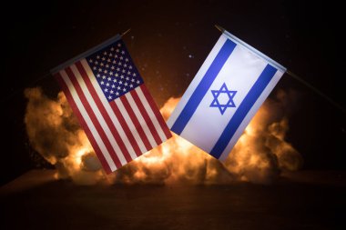 İsrail ve ABD 'de yanan karanlık arka planda küçük bayraklar. Savaş krizi kavramı ve uluslar arasındaki siyasi çatışmalar. Seçici odak