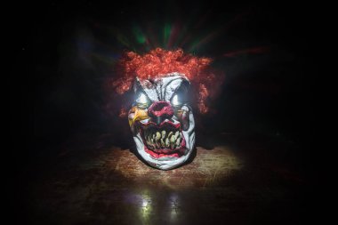 Tahta masadaki Ürkütücü Palyaço kafası. Karanlık sisli arka planda gülümseyen şeytani palyaço. Cadılar Bayramı konsepti Seçici odak