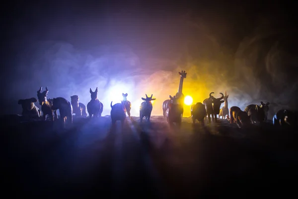 A group of animals are grouped together at foggy night with burning colorful background. Animals Running Escaping to Save Their Lives from fire. Selective focus.