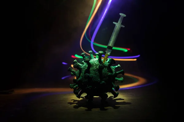 Corona virus Vaccine concept with syringe and green Corona virus novel miniature. Vaccine Concept of fight against coronavirus. Creative decoration with fog and backlight. Selective focus