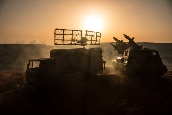 Творческое художественное оформление. Силуэт мобильного грузовика ПВО с радиолокационной антенной во время захода солнца. Ракетная установка нацелена на небо, готовое к атаке. Селективный фокус