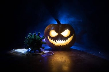 Corona virüsü küresel pandemik konsepti sırasında Cadılar Bayramı. Karanlıkta parlayan balkabakları ve Covid romanı tematik ürkütücü süslemelerle. Cadılar Bayramı balkabağı sisli arka planda. Seçici odak