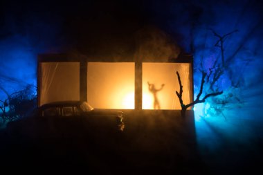 Sanat dekorasyonu. İçinde büyük pencereler ve zombiler olan eski bir ev. Penceredeki bulanık korkunç siluetler. Korku Cadılar Bayramı konsepti