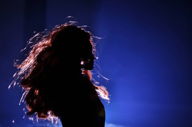 Hafif arka planda bir kadının silueti. Gece karanlığında uzun saçlı, sisli arka planda mavi ışıkları olan yalnız bir oyuncak bebek. Seçici odak