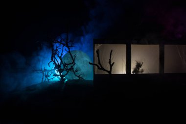 Sanat dekorasyonu. İçinde büyük pencereler ve zombiler olan eski bir ev. Penceredeki bulanık korkunç siluetler. Korku Cadılar Bayramı konsepti