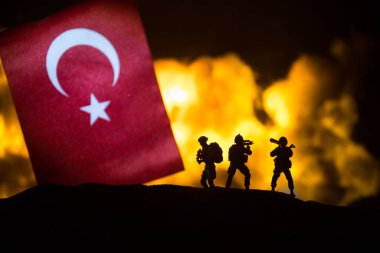 Yanan karanlık arka planda küçük bir hindi bayrağı. Savaş krizi kavramı ve uluslar arasındaki siyasi çatışmalar. Türk bayrağına karşı silahlı asker silueti. Seçici odak