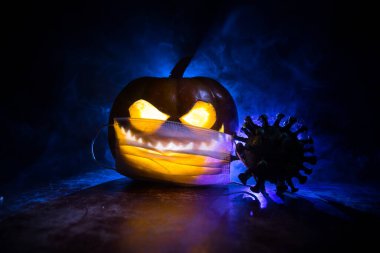 Corona virüsü küresel pandemik konsepti sırasında Cadılar Bayramı. Karanlıkta parlayan balkabakları ve Covid romanı tematik ürkütücü süslemelerle. Cadılar Bayramı balkabağı sisli arka planda. Seçici odak