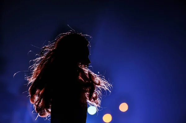 Silhouette of a female face on a light background. SIlhouette of a lonely doll with long hair at night blue lights on foggy background. Selective focus