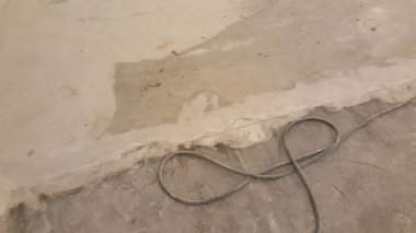 Beton zeminin bir bölümünde düzgün olmayan bölgelere uygulanan yeni yama malzemesi ile onarım çalışmaları görülüyor ve yakınlarda kalın bir elektrik kablosu var.