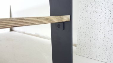 Çağdaş mobilya inşaatı, katmanlı ahşap element ile mat siyah metal desteği arasındaki güvenli bağlantıyı gösteriyor.
