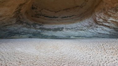 Mağaranın içi katmanlı kaya katmanlarını ve küçük, desenli çakıl taşları ya da kumla kaplı zemini ortaya çıkarır.