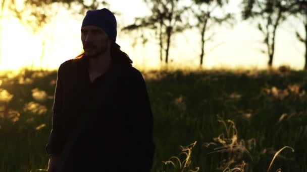 Un hombre camina en un campo al atardecer — Vídeos de Stock