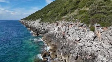 Uçağı Rocky Coastline 'a yaklaşıyor. Dalgalar Kayalıklara Çarpıyor. İnsansız hava aracı kıyı şeridine doğru uçuyor ve sonra geri dönüyor. Turkuaz su, kayalık sahil ve kıyı üzerindeki yeşil tepelerle dramatik deniz manzarasını gözler önüne seriyor..