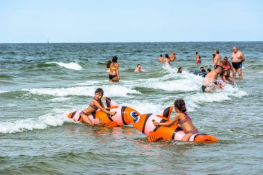 LEBA, POLAND - 31 Temmuz 2016: Şişme oyuncaklarla deniz suyunda oynayan iki küçük kız, yaz tatilinde sahilde eğlenen mutlu insanlar