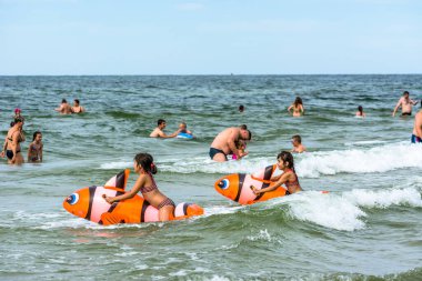 LEBA, POLAND - 31 Temmuz 2016: Şişme oyuncaklarla deniz suyunda oynayan iki küçük kız, yaz tatilinde sahilde eğlenen mutlu insanlar