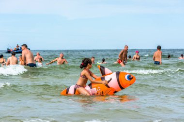 LEBA, POLAND - 31 Temmuz 2016: Küçük kız şişme oyuncaklarla deniz suyunda oynuyor, mutlu insanlar yaz tatilinin tadını çıkarıyor