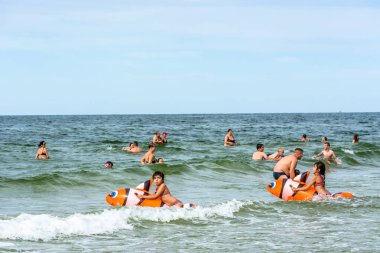 LEBA, POLAND - 31 Temmuz 2016: Şişme oyuncaklarla deniz suyunda oynayan iki küçük kız, yaz tatilinde sahilde eğlenen mutlu insanlar