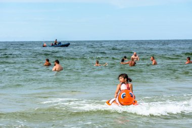 LEBA, POLAND - 31 Temmuz 2016: Küçük kız şişme oyuncaklarla deniz suyunda oynuyor, mutlu insanlar yaz tatilinin tadını çıkarıyor