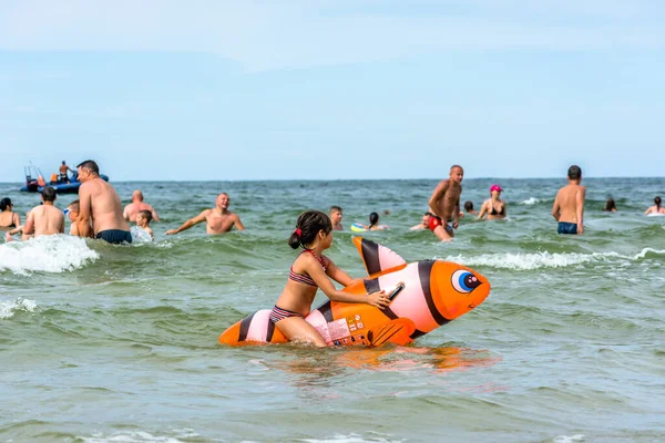 LEBA, POLAND - 31 Temmuz 2016: Küçük kız şişme oyuncaklarla deniz suyunda oynuyor, mutlu insanlar yaz tatilinin tadını çıkarıyor