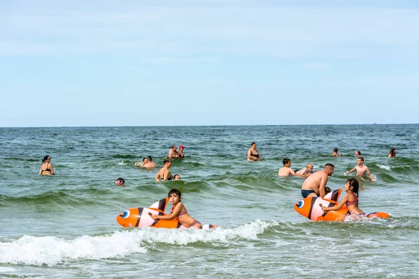 LEBA, POLAND - 31 Temmuz 2016: Şişme oyuncaklarla deniz suyunda oynayan iki küçük kız, yaz tatilinde sahilde eğlenen mutlu insanlar