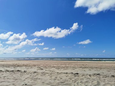 Kuzey Denizi 'nin dalgalarıyla panoramik kumlu sahil ve güneşli bir günde dağınık bulutlu açık mavi gökyüzü.