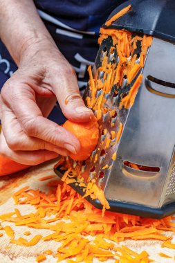 Paslanmaz çelik rendesinin üzerinde taze, sulu havuç rendeleyen kadın eli.