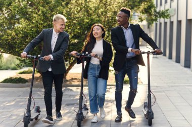 İş projesinin detaylarını tartışan neşeli çok ırklı meslektaşlar elektrikli scooterlarla ofise gidin.