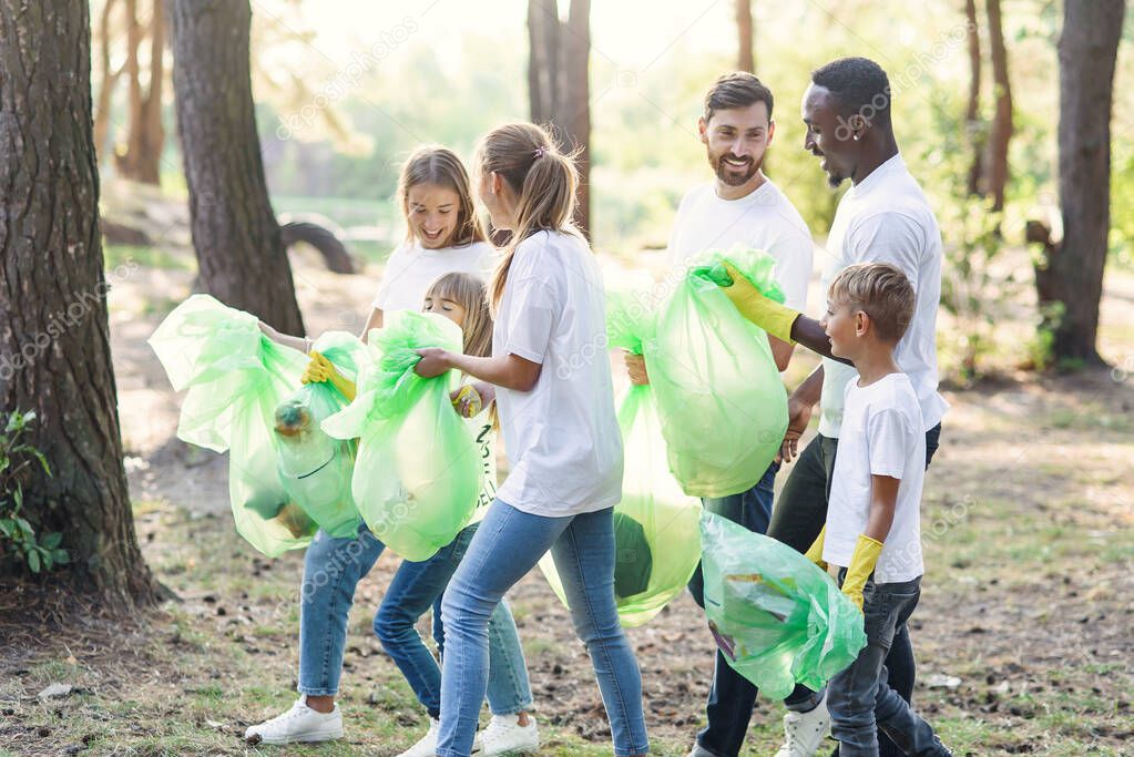 Active team of international nature lovers in white t-shirs collecting rubbish into plastic packs at forest.