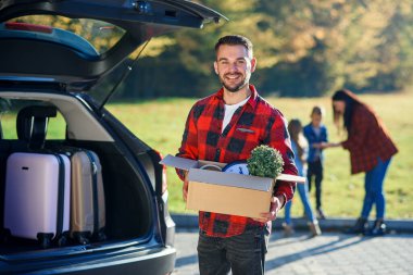 Genç bir adam, yeni bir eve taşındıktan sonra aile arabasının bagajlarını boşaltan karton bir kutu tutuyor..