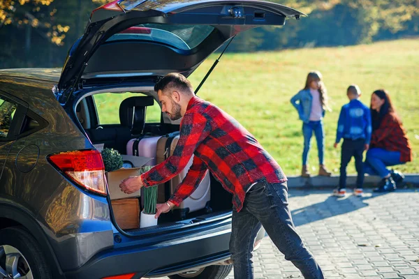 Bonito pai barbudo carrega bagagem no porta-malas do carro indo em uma viagem de férias em família. — Fotografia de Stock