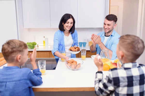 Joyful family of four persons drink orange juice with croissants and tasty cakes in the kitchen. Happy family concept.