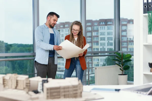 Diseñador masculino barbudo experimentado y su colega mujer con rastas analizando planos de proyectos futuros. — Foto de Stock