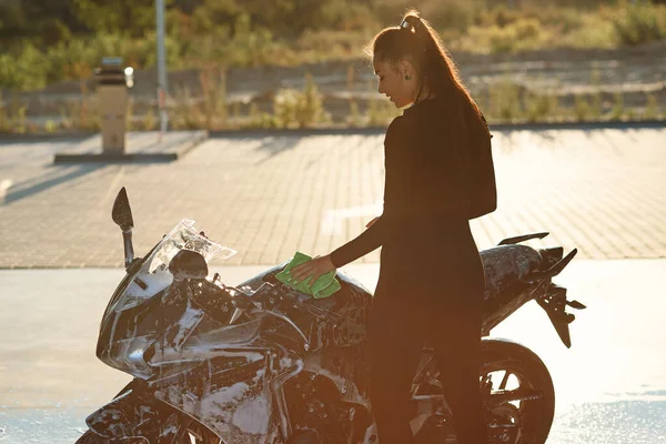 Verführerische junge Frau wäscht stylisches Sportmotorrad und wischt es aus lila Schaum. Sorge um das Fahrzeug. — Stockfoto