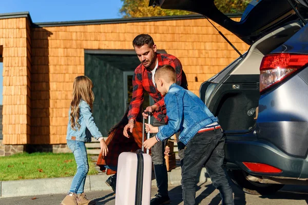 Uma família feliz desempacota bagagem do porta-malas de um carro depois de se mudar para uma nova casa. — Fotografia de Stock