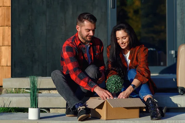 Pareja joven sentada en escaleras divirtiéndose desempacando cajas después de mudarse a nueva casa. — Foto de Stock