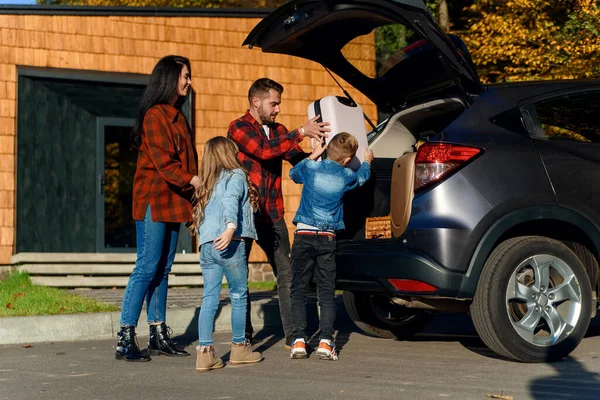 Счастливая семья загружает багаж в багажник автомобиля во время семейного отдыха. Лицензионные Стоковые Фото