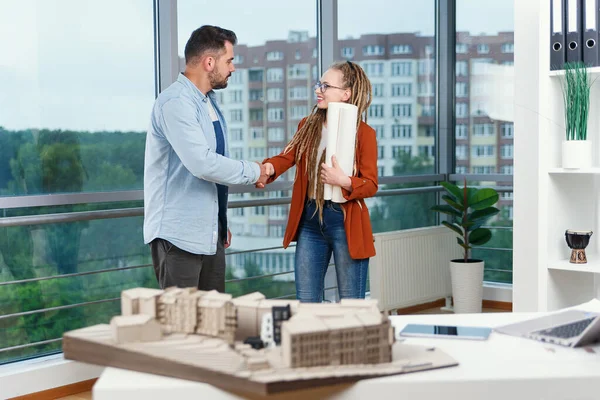 Experienced satisfied designers discussing project details using blueprint of building and handshaking each other. — Stock Photo, Image