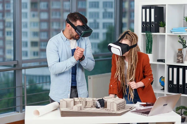 Пара дизайнеров или инженеров анализируют макет будущего жилого района, используя защитные очки в архитектурном бюро. Стоковая Картинка
