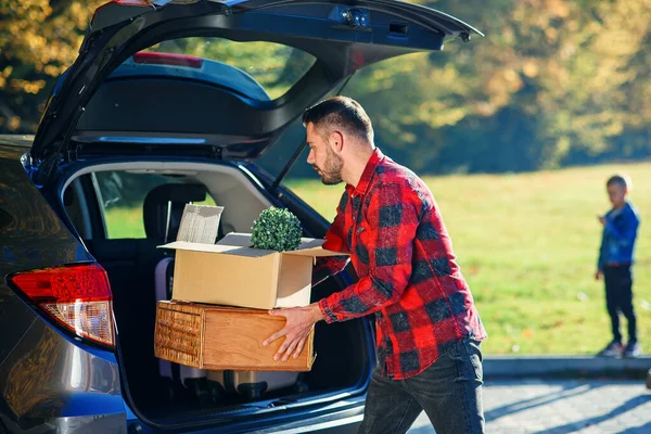 Handsome trendy bearded man loads luggage into the car trunk going on a family vacation trip. — Stock Photo, Image