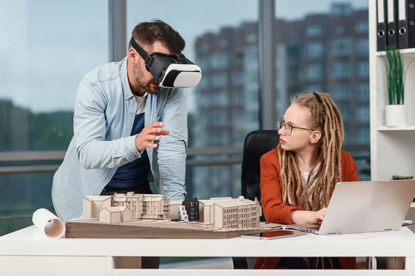 Arquiteto masculino profissional em óculos de realidade aumentada trabalhando com simulador de construção e mulher colega de trabalho com laptop — Fotografia de Stock