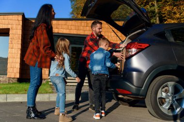 Yeni bir eve taşınmadan ya da tatile çıkmadan önce mutlu bir aile bavulunu bir arabanın bagajına koyar..