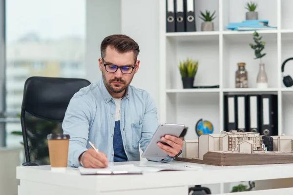 Erfaren manlig arkitekt på kontoret inspekterar projekt bostadskomplex och gör beräkningar med hjälp av en surfplatta PC. — Stockfoto