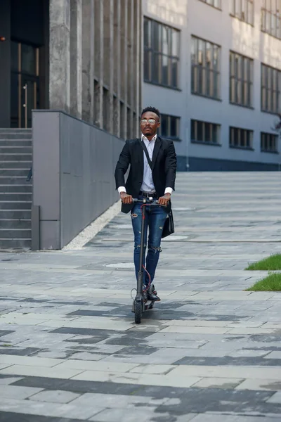 Moderno hombre de negocios negro alegre monta scooter eléctrico después de terminar su día de trabajo en la oficina. — Foto de Stock