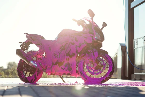 Motocicleta esportiva elegante com espuma roxa na lavagem de carro self-service ao nascer do sol. — Fotografia de Stock