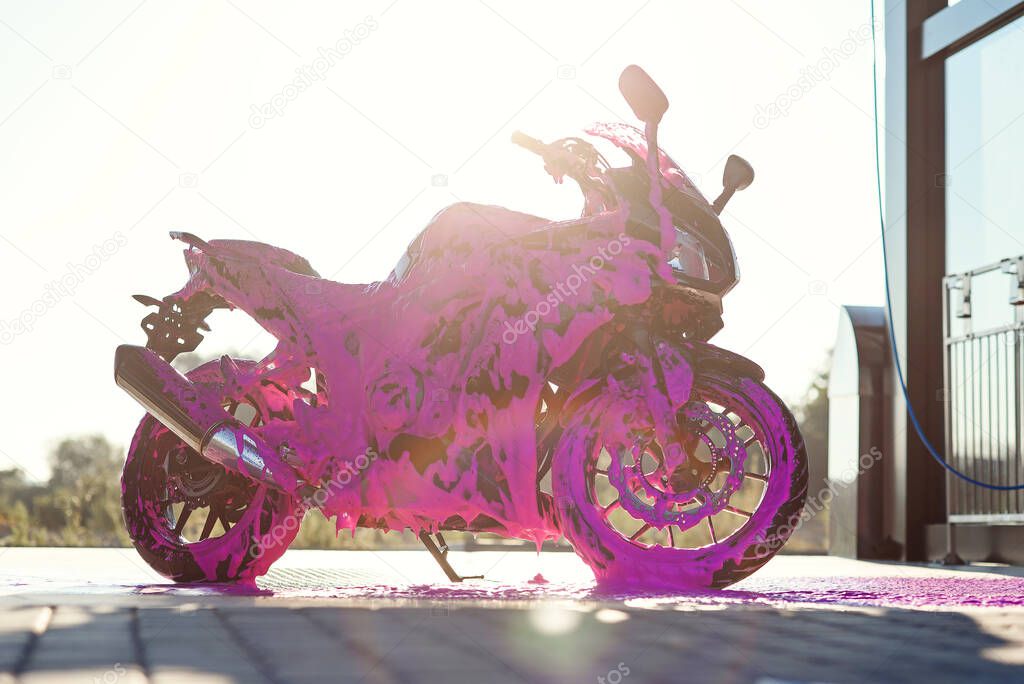 Stylish sports motorcycle with purple foam on the self-service car wash at sunrise.
