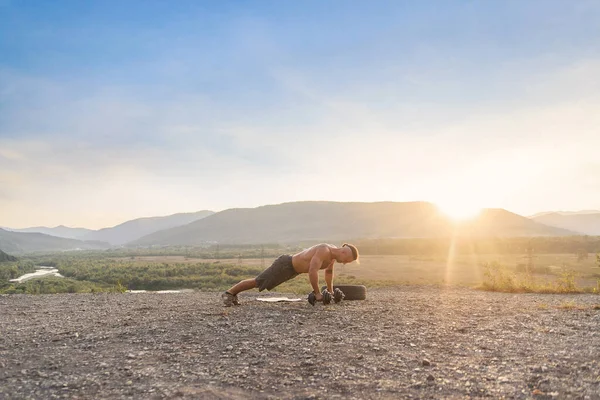 Atlético joven haciendo flexiones al aire libre en la colina de la montaña al atardecer. — Foto de Stock