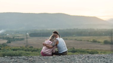 Genç adam gün batımında dağın zirvesinde kız arkadaşına sarılıyor..