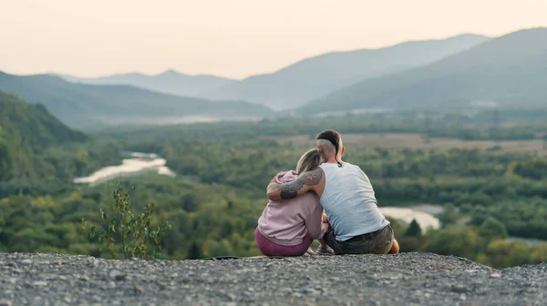 Young man hugs his girlfriend on the mountain peak at sunset background. — Stock Photo, Image