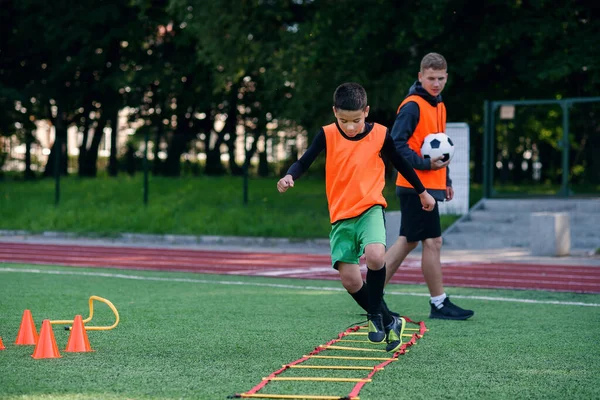 Мотивированные подростки-футболисты выполняют беговые упражнения с преодолением препятствий, применяя стойки на искусственном футбольном поле. — стоковое фото