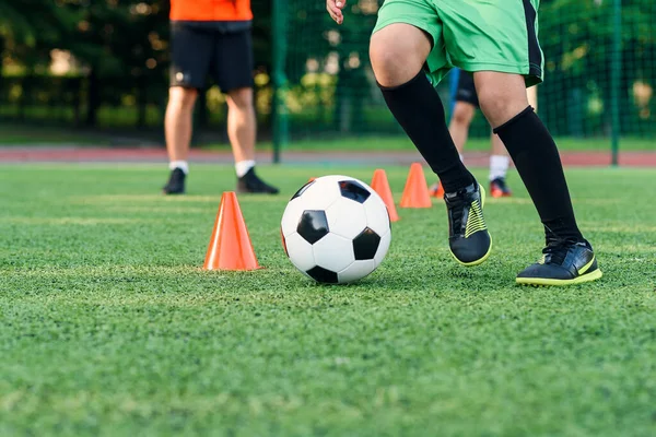 近身男孩穿着运动服在足球场上训练足球，并学习在训练橙色球果之间打圈. — 图库照片